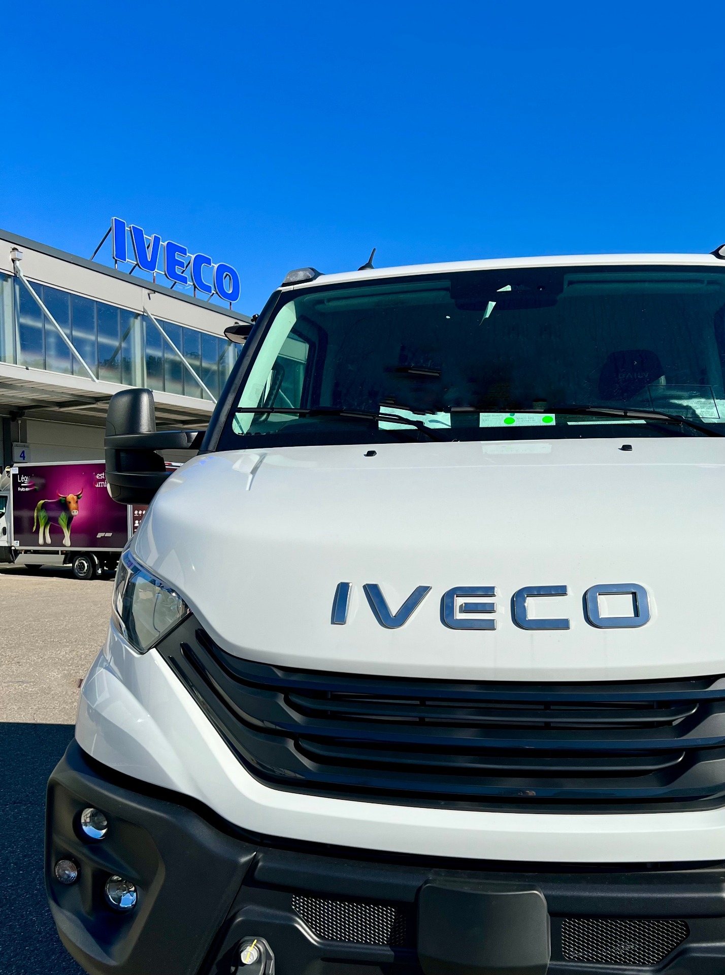 Vorderansicht eines weißen Iveco-Fahrzeugs vor einer Werkstatt mit blauem Firmenschild und Glasfassade.